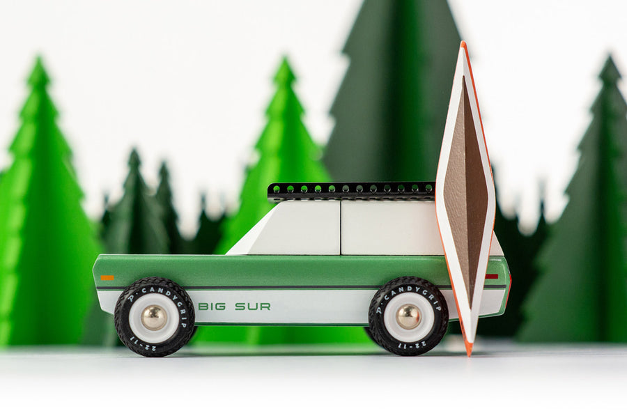 Side of the Candylab Big Sur car toy with a wooden kayak toy in front of some green wooden trees