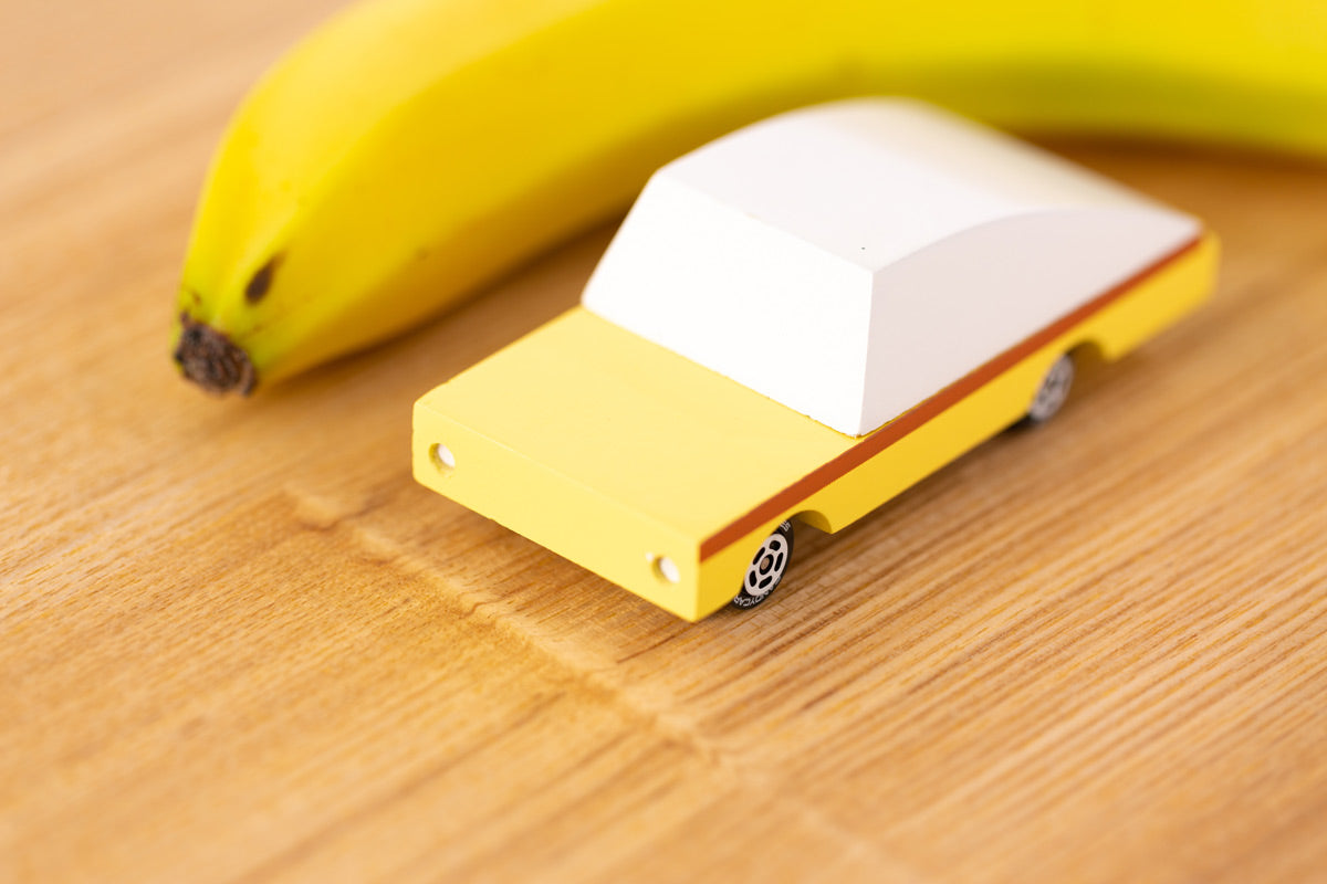 Close up of the Candylab wooden banana car toy on a wooden table next to a banana