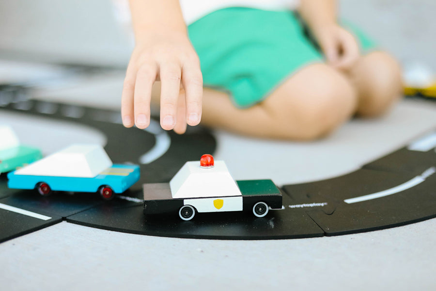 Close up of a childs hand pushing the candylab handmade wooden police car on a black rubber road