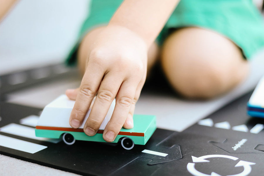 Close up of a childs hand pushing the Candylab solid wooden teal wagon toy on a black road set