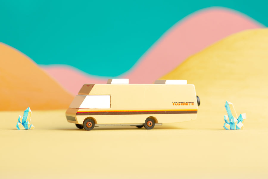 Candylab childrens diecast wooden campervan toy on a yellow background in front of some orange and pink hills