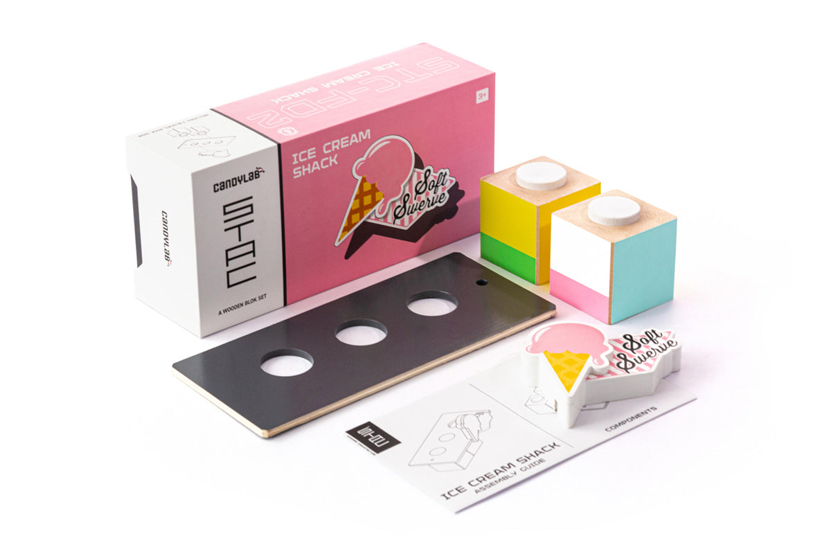 Pieces of the Candylab handmade wooden ice cream shack set on a white background next to the pink box