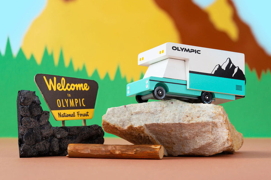 Candylab wooden campervan toy on top of a grey rock in front of a colourful mountain background