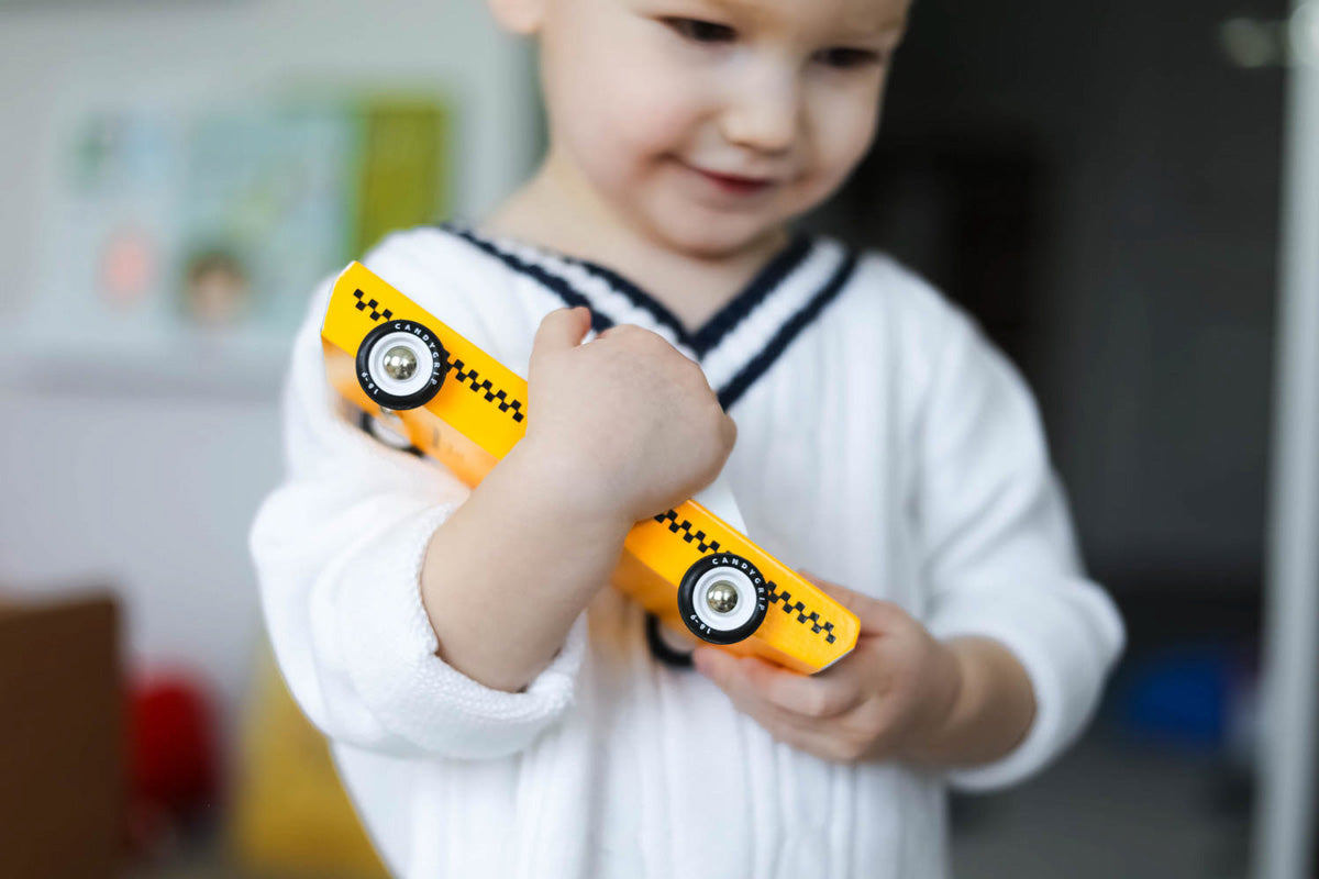 Close up of a young boy in a white jumper holding a Candylab solid wooden taxi cab diecast car toy