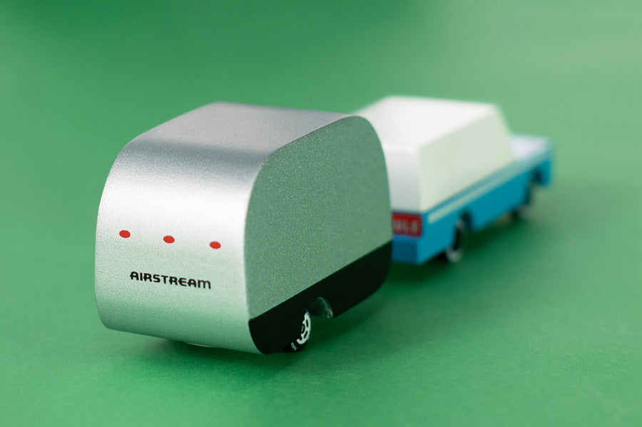 Close up of the Candylab small wooden Airstream toy connected to a blue car toy on a green background