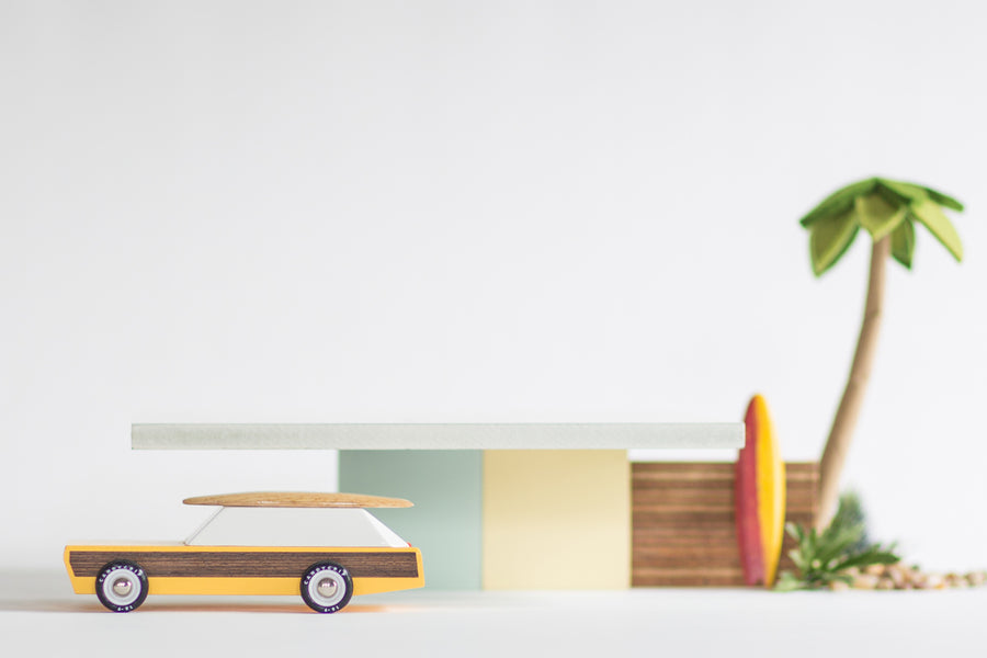 Candylab solid wooden car toy in front of a miniature waldorf shack in some wooden surfboards