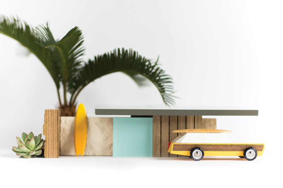 Candylab childrens wooden diecast car toy in front of a small wooden shack model and palm tree