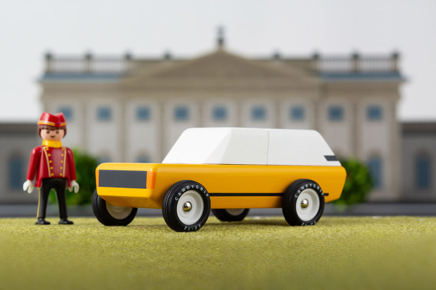 Toy figure stood on a green background next to the Candylab childrens handmade cotswold suv toy car