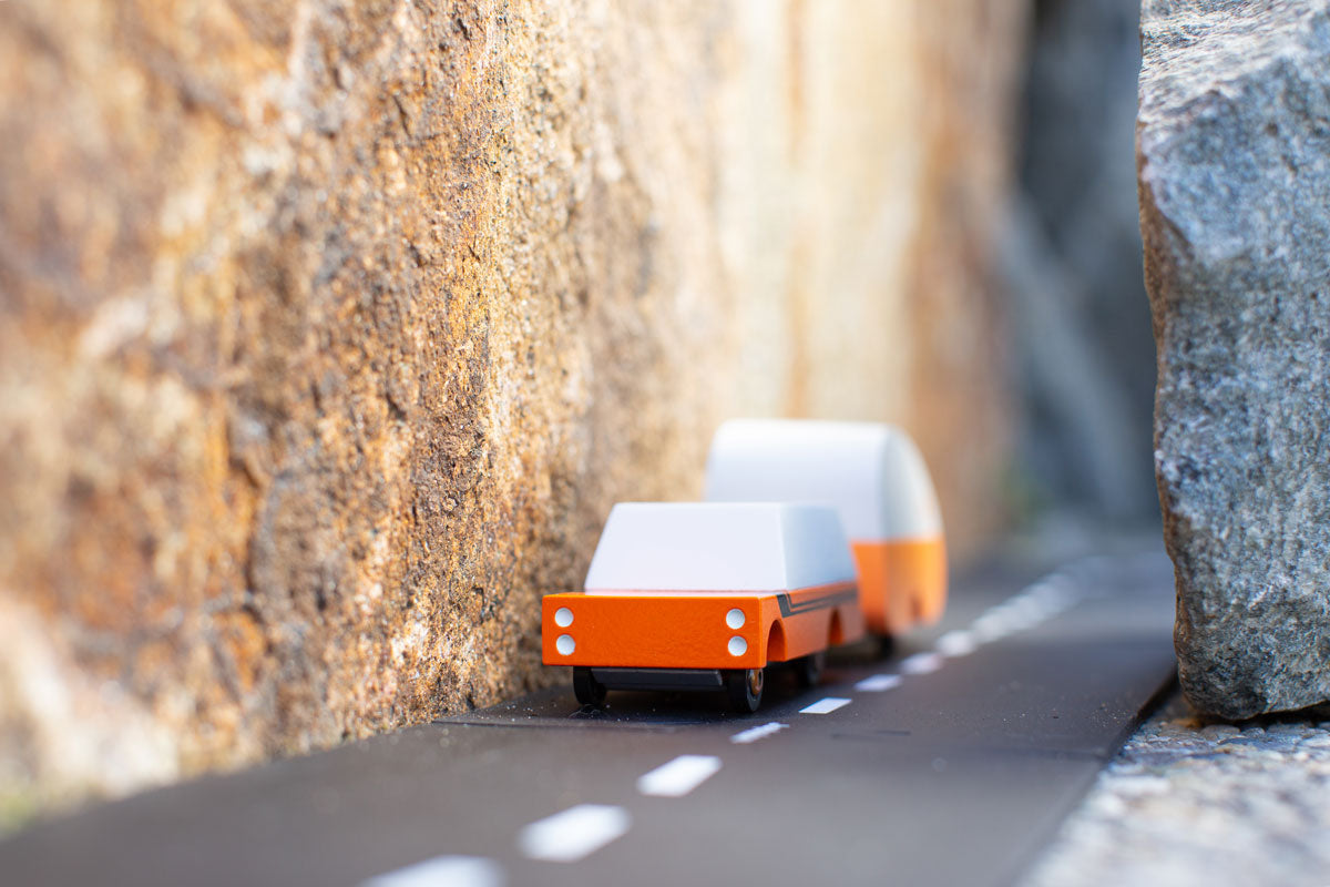 Candylab orange wooden suv toy pulling an orange caravan toy between two large rocks