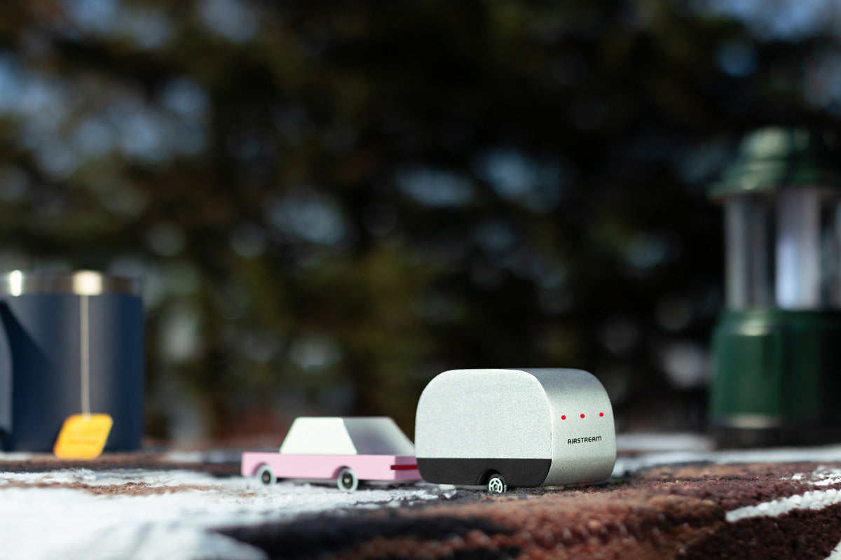 Close up of a childrens candylab airstream and pink sedan toy on a brown blanket in front of a camping mug and lamp