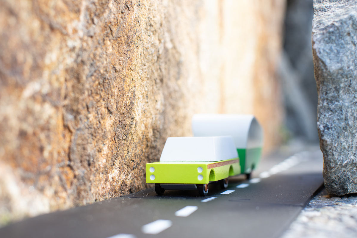 Green candylab suv car toy pulling a little caravan on a rubber road between 2 rocks