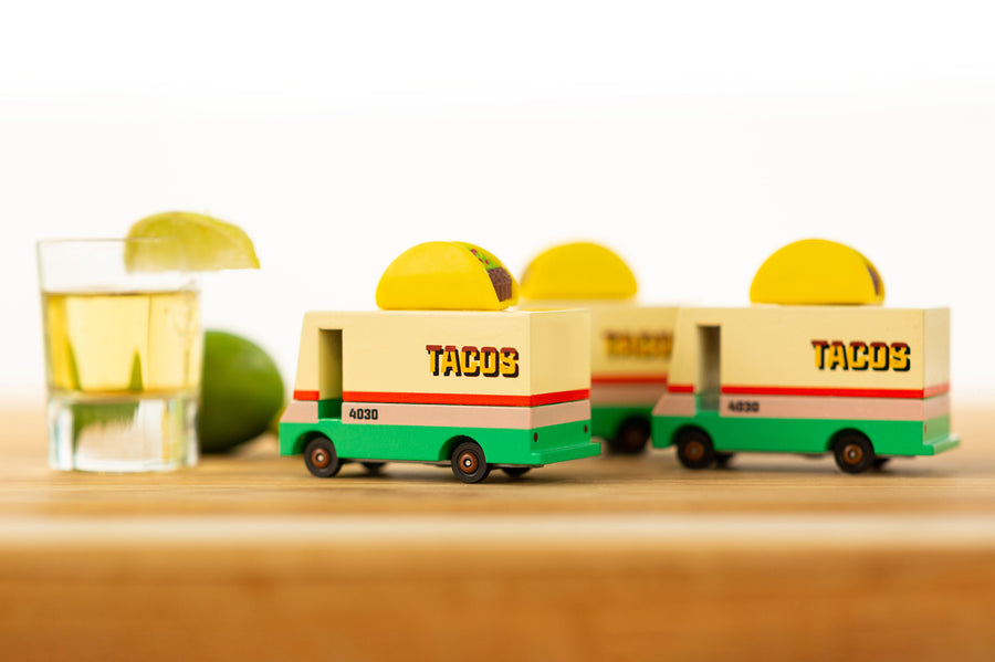 Close up of 3 wooden Candylab taco vans on a wooden table next to a glass