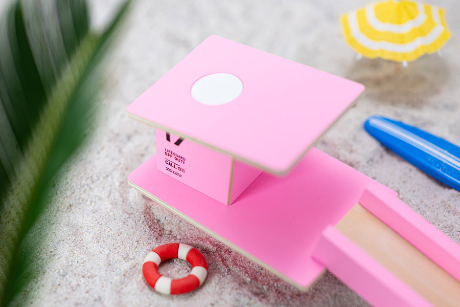 Close up of the Candylab slotting wooden beach tower toy on a sandy background next to some miniature umbrellas