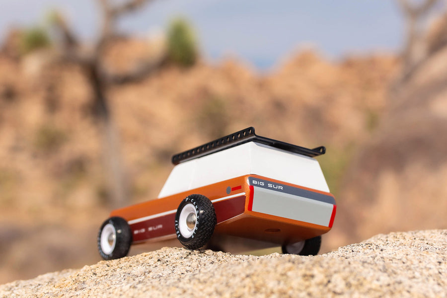 Close up of the Candylab solid wooden big sur car toy on a large rock in front of a beige background