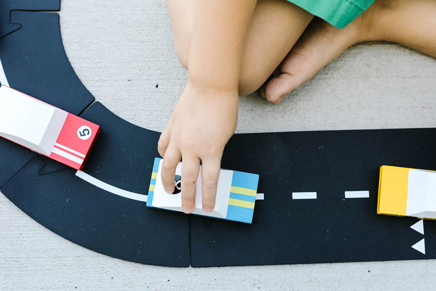 Close up of a child pushing the Candylab eco-friendly wooden racing car toy on a road set