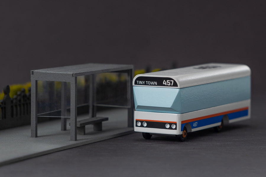 Candylab Tiny Town toy bus on a grey background next to a miniature bus stop