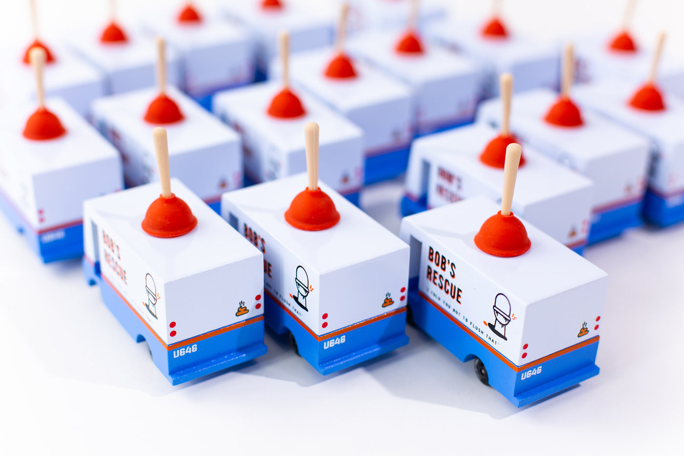 Group of Candylab handmade wooden plumbing truck toys lined up on a white background