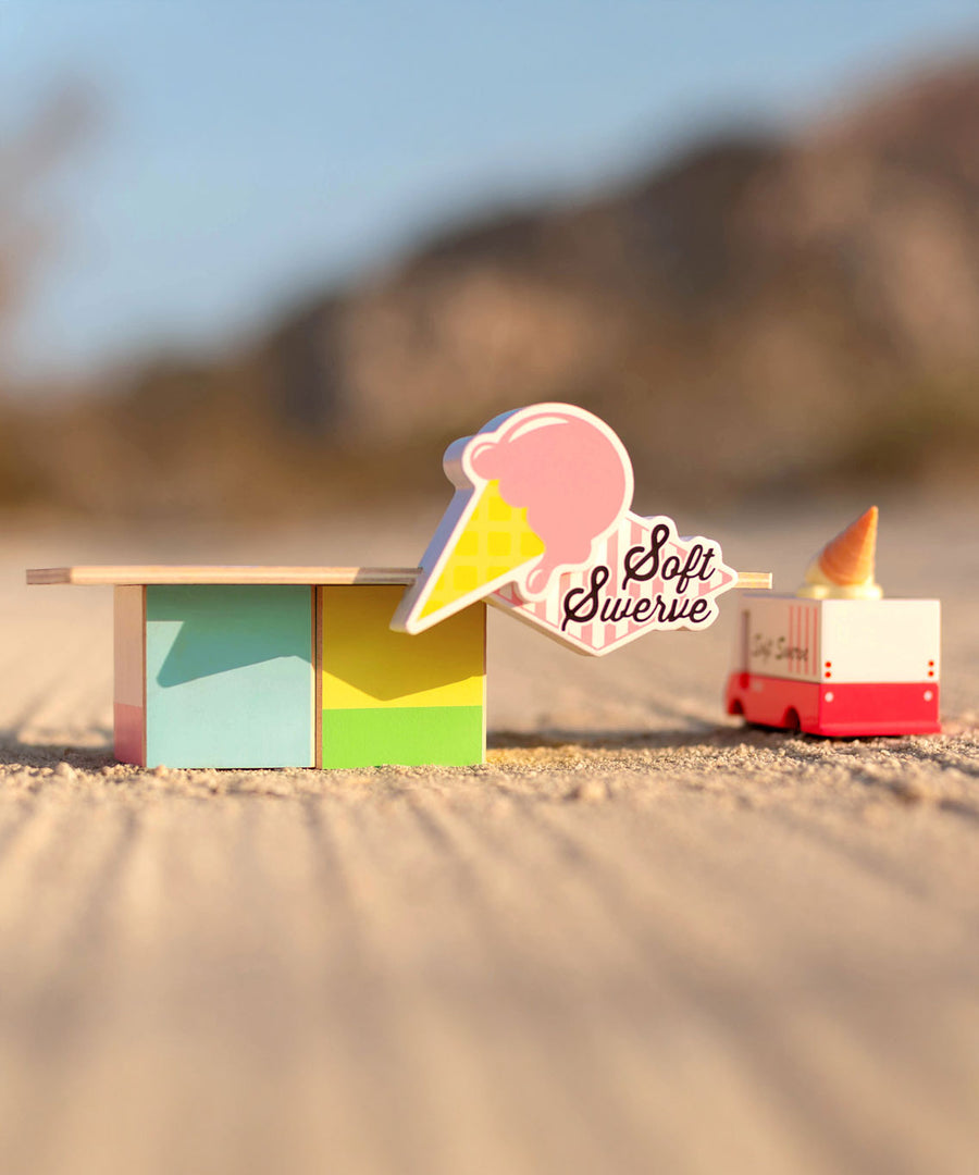 The Candylab Ice Cream Food Shack next to a ice cream truck on a sandy surface.