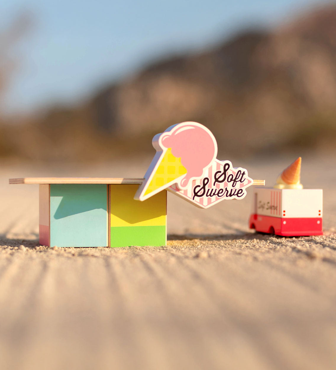 The Candylab Ice Cream Food Shack next to a ice cream truck on a sandy surface.