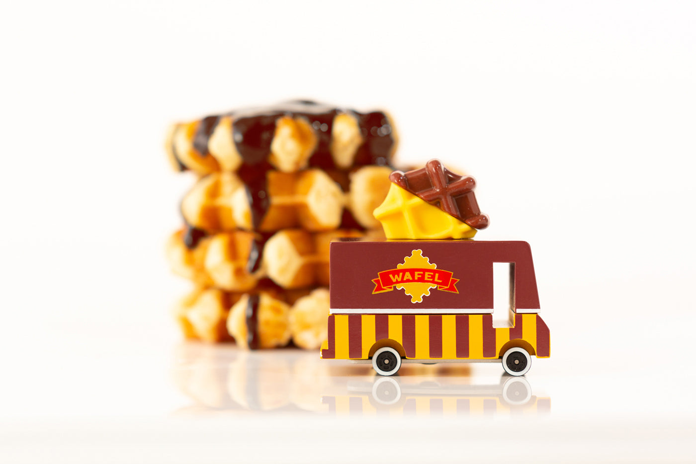 Close up of the Candylab wooden waffle toy truck next to a pile of chocolate waffles on a white background