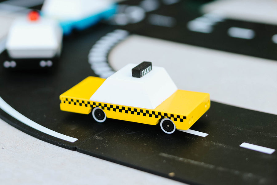 Close up of the Candylab wooden taxi toy vehicle on a black toy road set