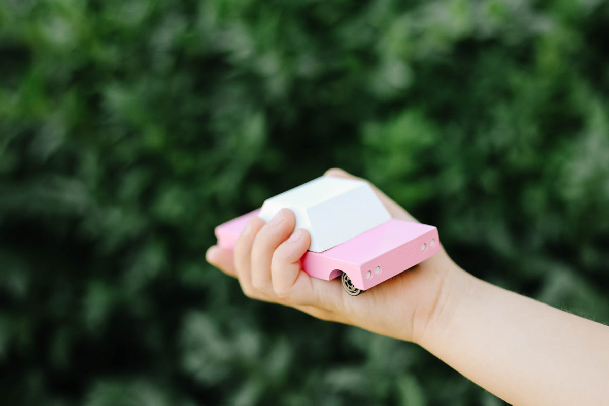 Close up of a childs hand holding the Candylab solid wooden pink sedan car on a green background