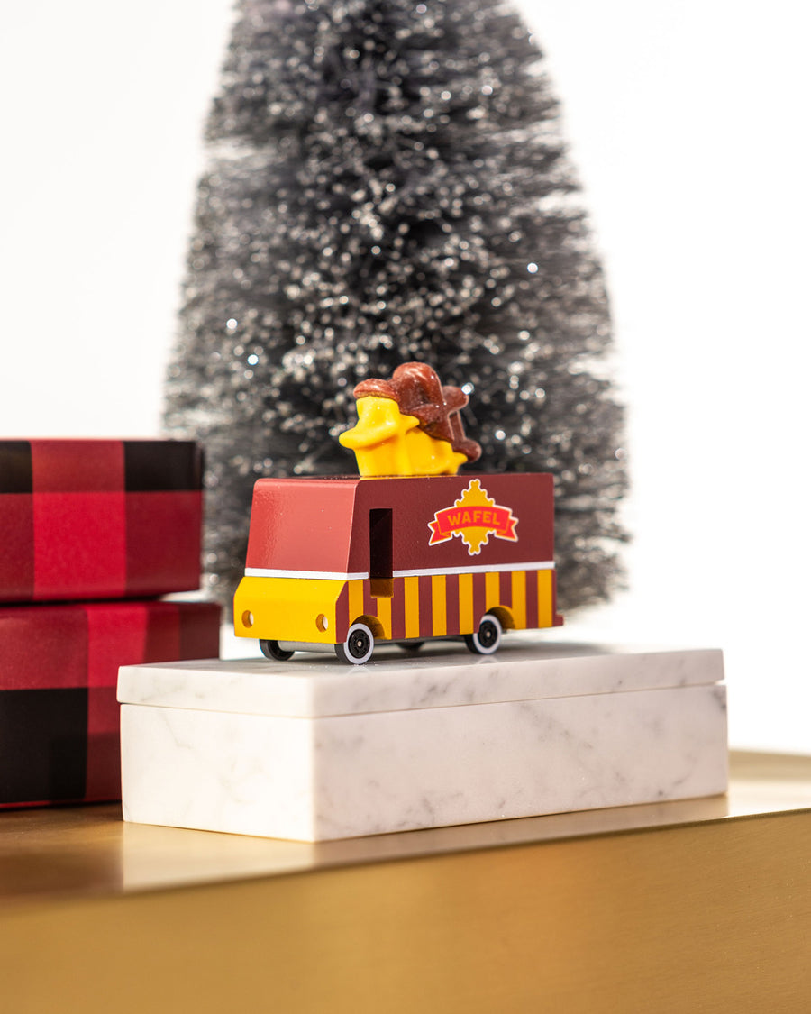 Candylab wooden candyvan waffle truck on a pile of presents in front of a Christmas tree