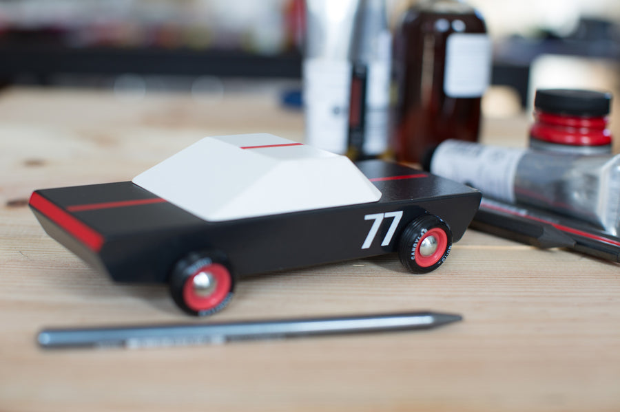 white and red race car toy on a white shelf next to other Candylab cars and some children's drawings