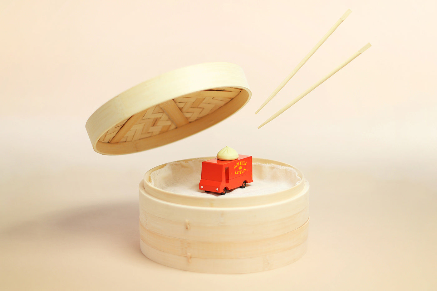 Candylab wooden dumpling toy truck inside a round wooden box next to some chopsticks on a beige background