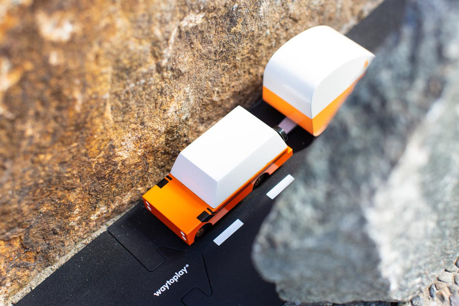 Orange suv diecast toy car pulling an orange caravan toy between two large rocks