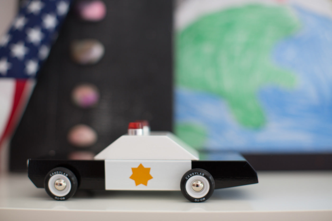 Side of the Candylab childrens diecast wooden toy on a white worktop in front of a blue and green background