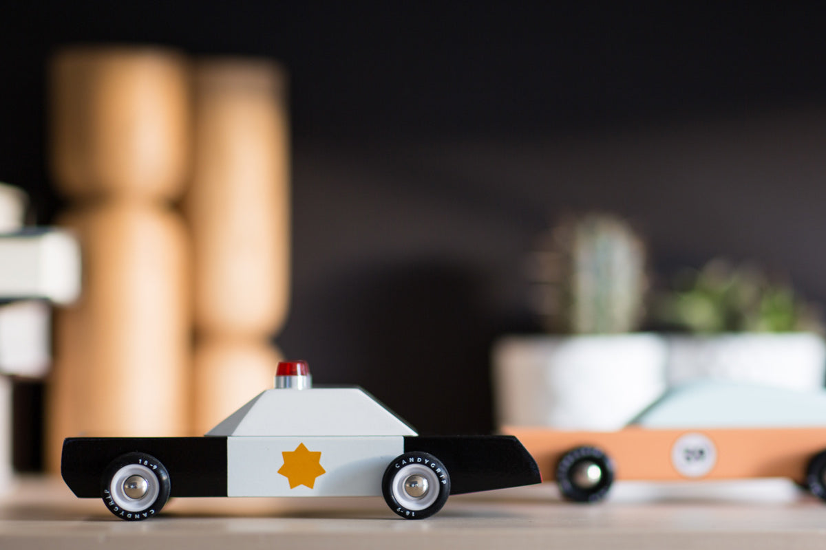 Candylab wooden collectable police cruiser toy on a wooden table in front of a black background