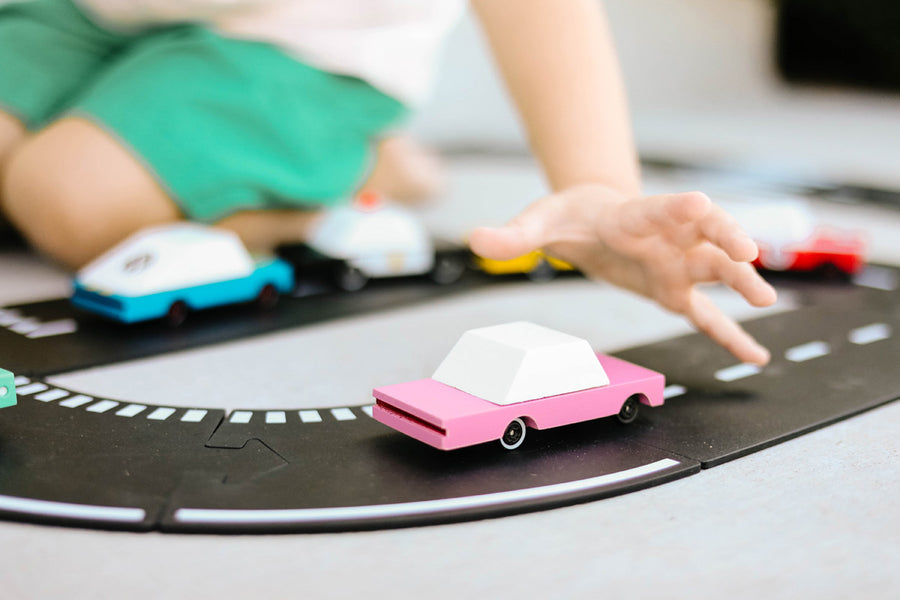 Close up of childs hand reaching for the Candylab handmade wooden pink sedan candycar on a play road set