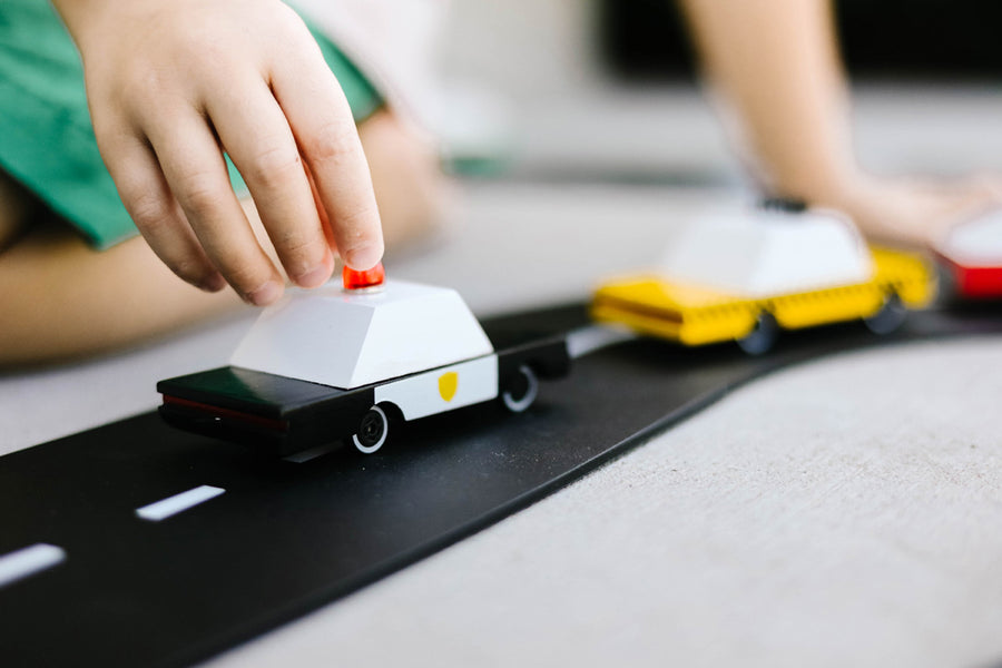 Close up of a childs hand pushing the candylab candycar police vehicle on a black rubber road