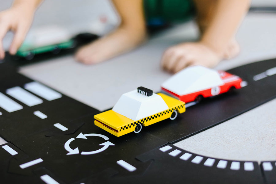 Close up of a child playing with the Candylab wooden taxi toy car on a black toy road set