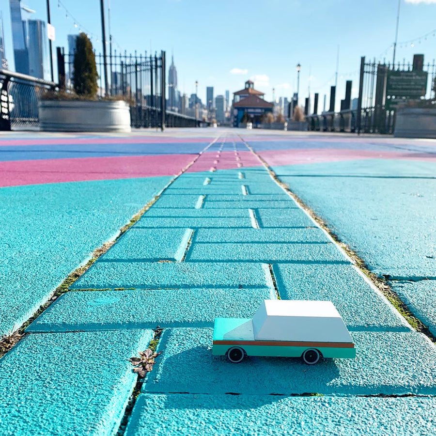 Candylab teal wagon toy car on a blue brick floor in front of a cityscape