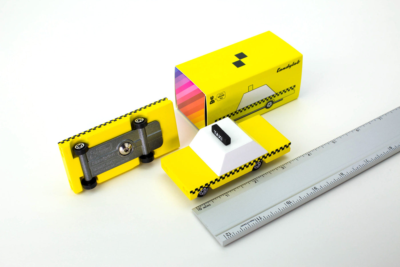 Candylab childrens wooden toy taxi on a white background next to a metal ruler and its yellow box