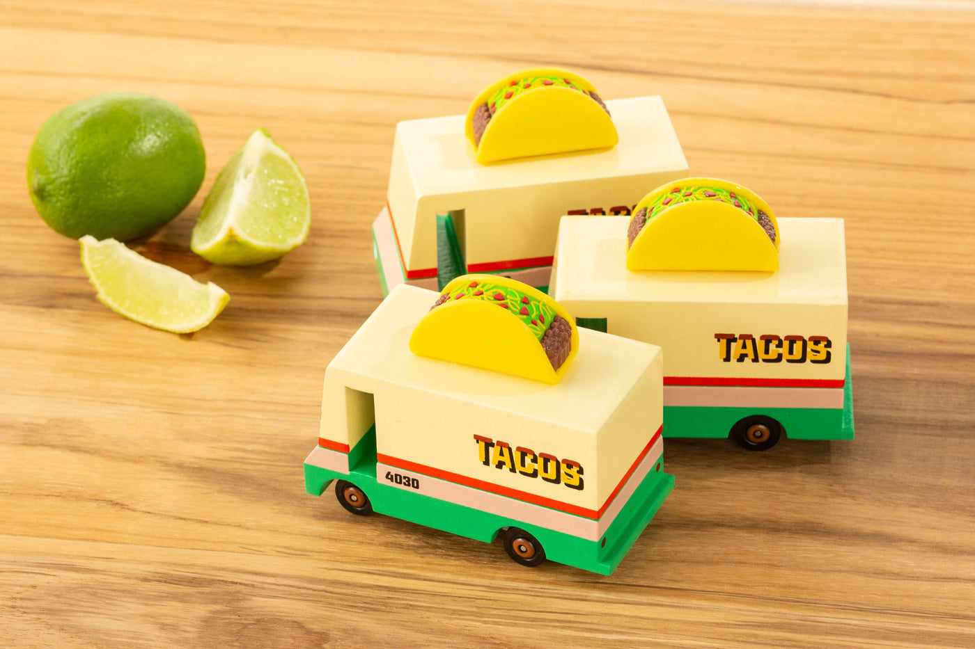 3 Candylab solid wooden taco van toys on a wooden chopping board next to a sliced lime