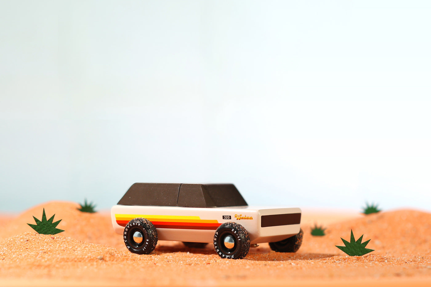 Candylab children's handmade wooden Wanderer car toy on some sand on a light blue background