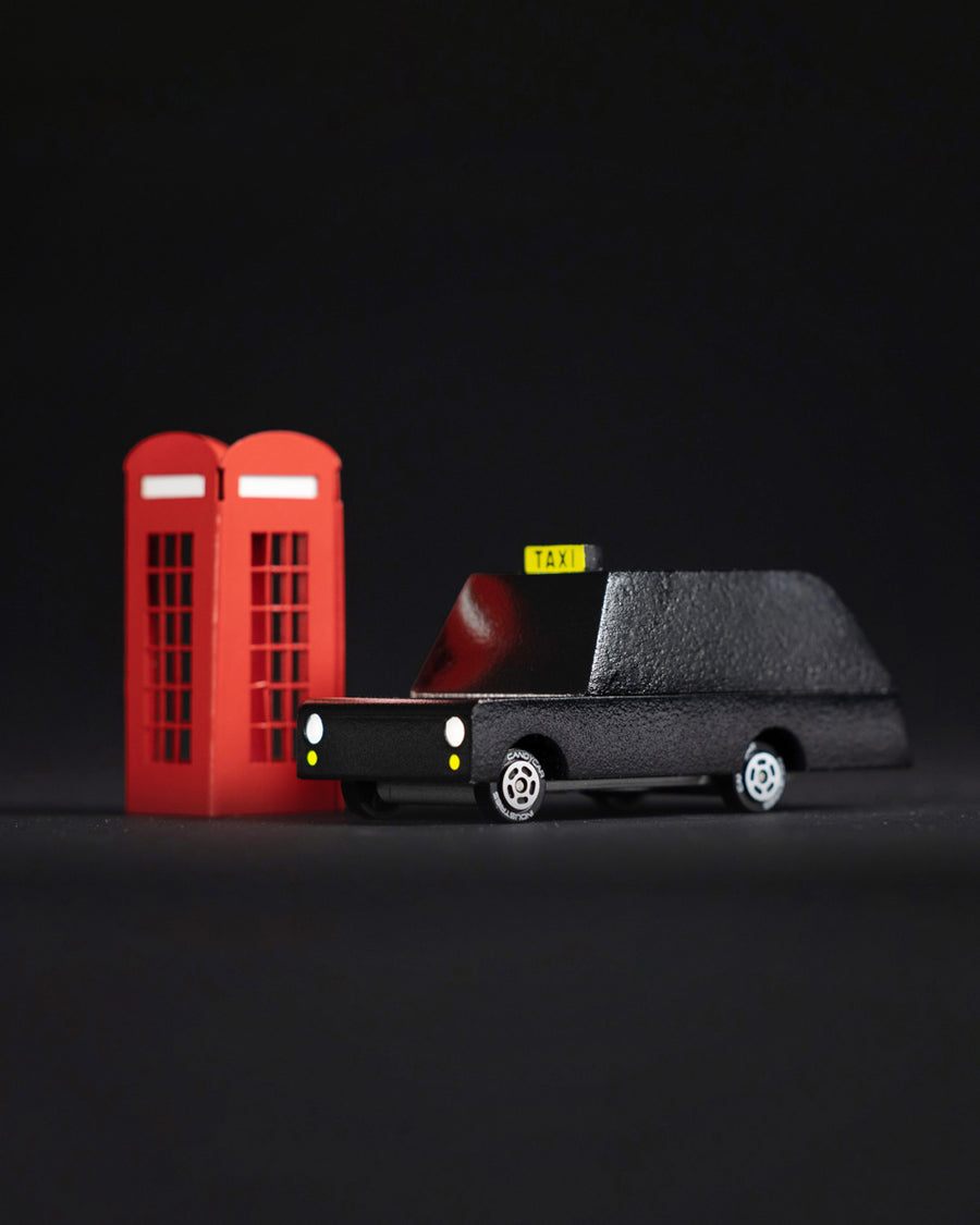 Candylab wooden London taxi car toy on a white snow scene background next to some miniature trees and red phonebox