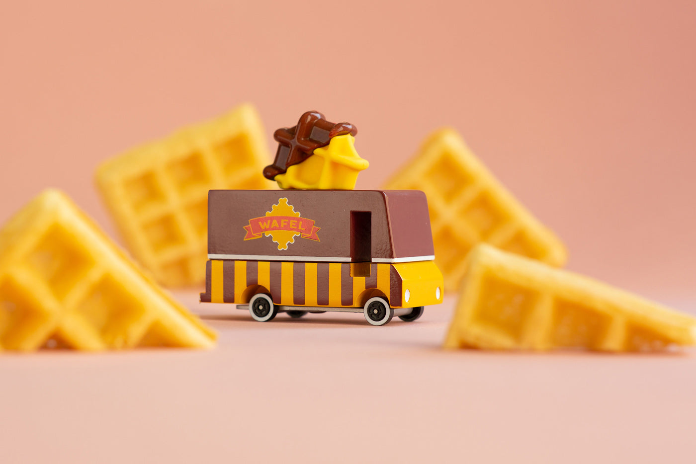 Candylab toy waffle truck on a pink background next to pieces of waffle