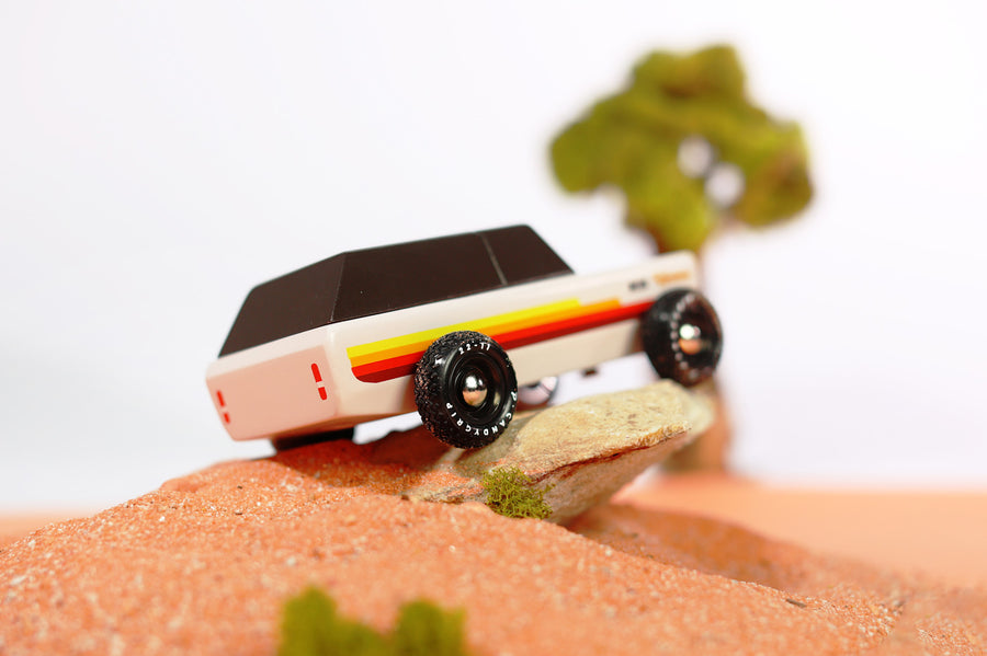 Close up of the Candylab wooden Wanderer SUV car toy on a small rock in some sand