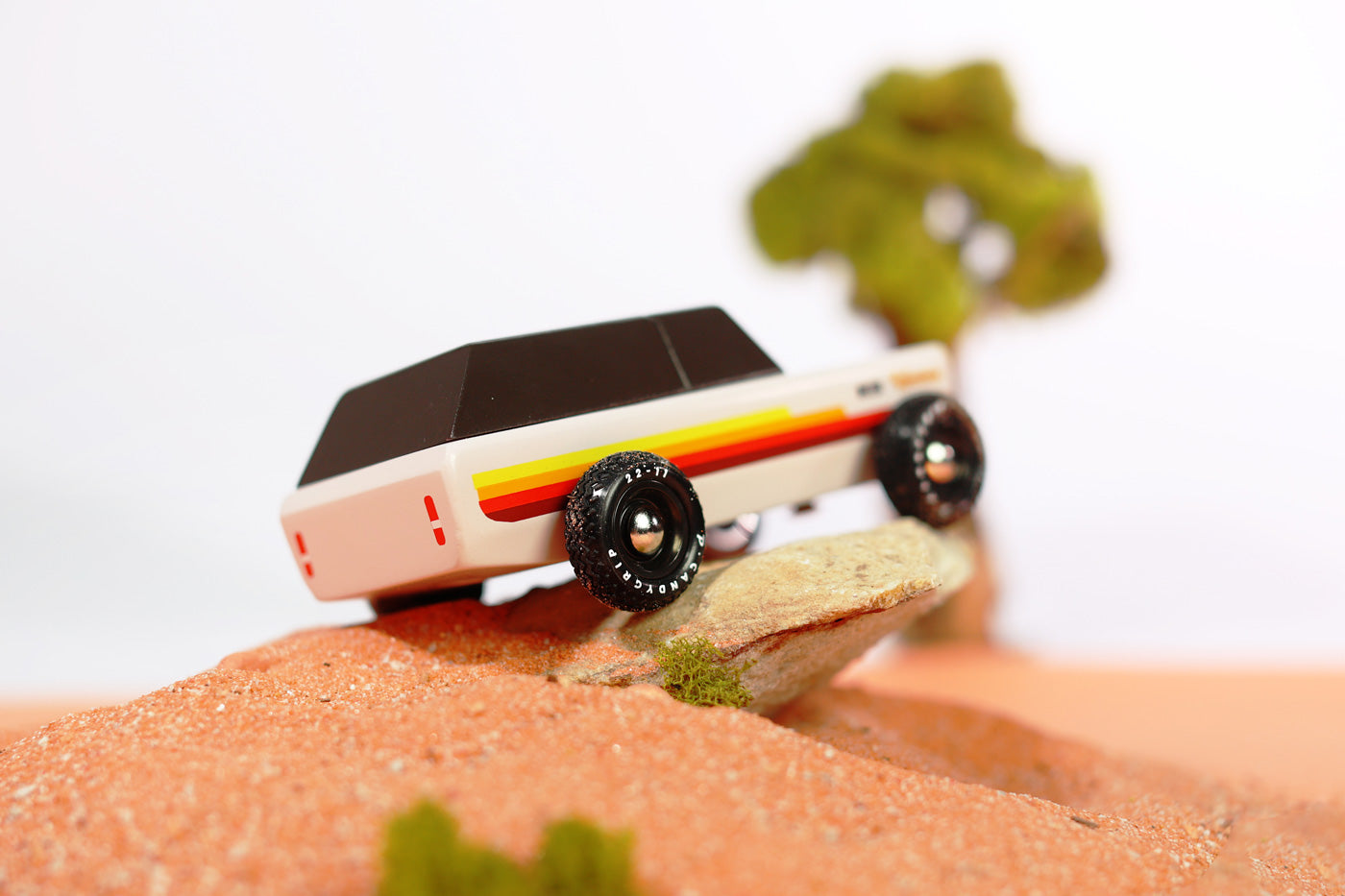 Close up of the Candylab wooden Wanderer SUV car toy on a small rock in some sand