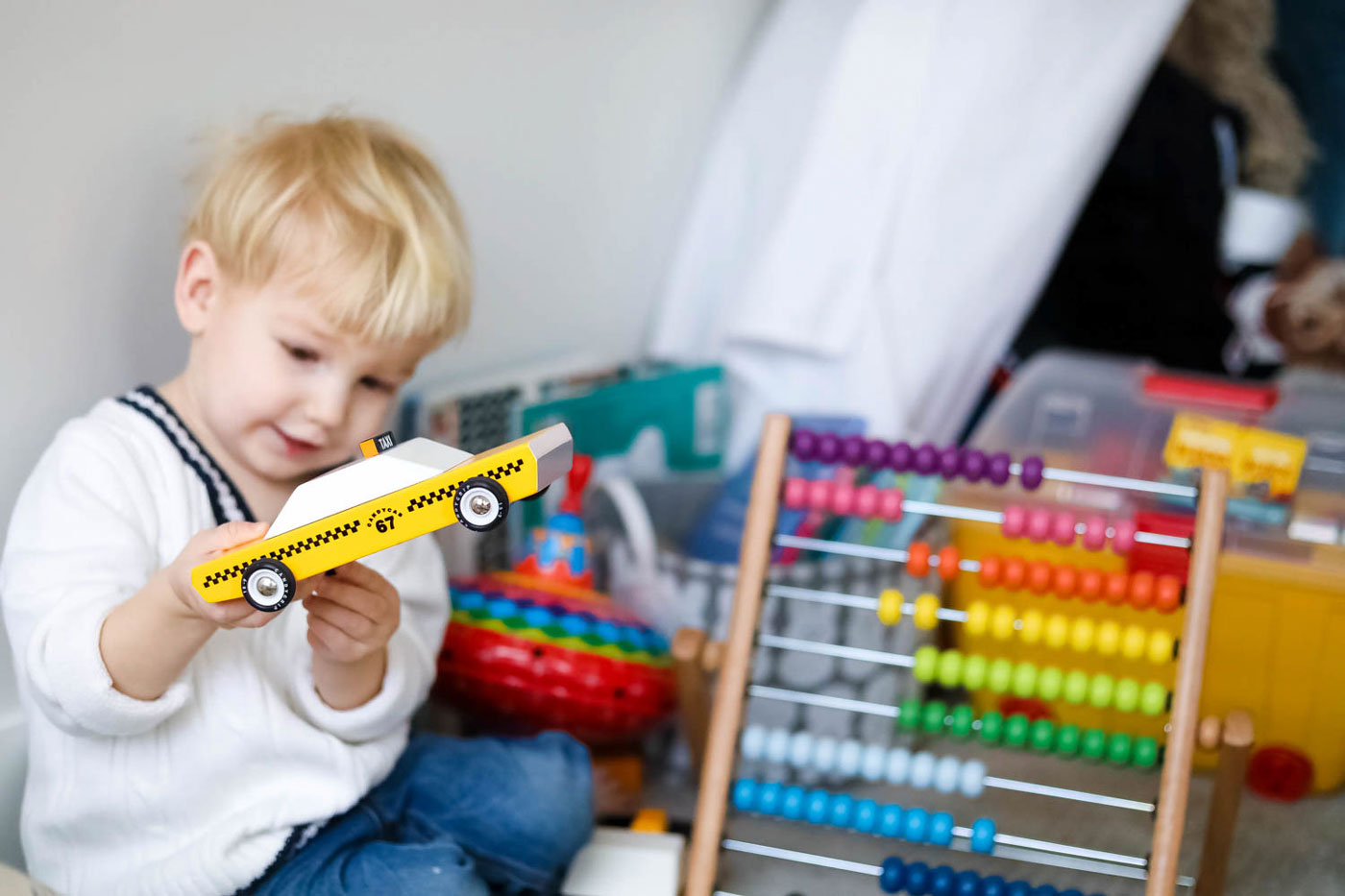 Young child holding a Candylab wooden taxi cab toy next to a rainbow wooden abacus