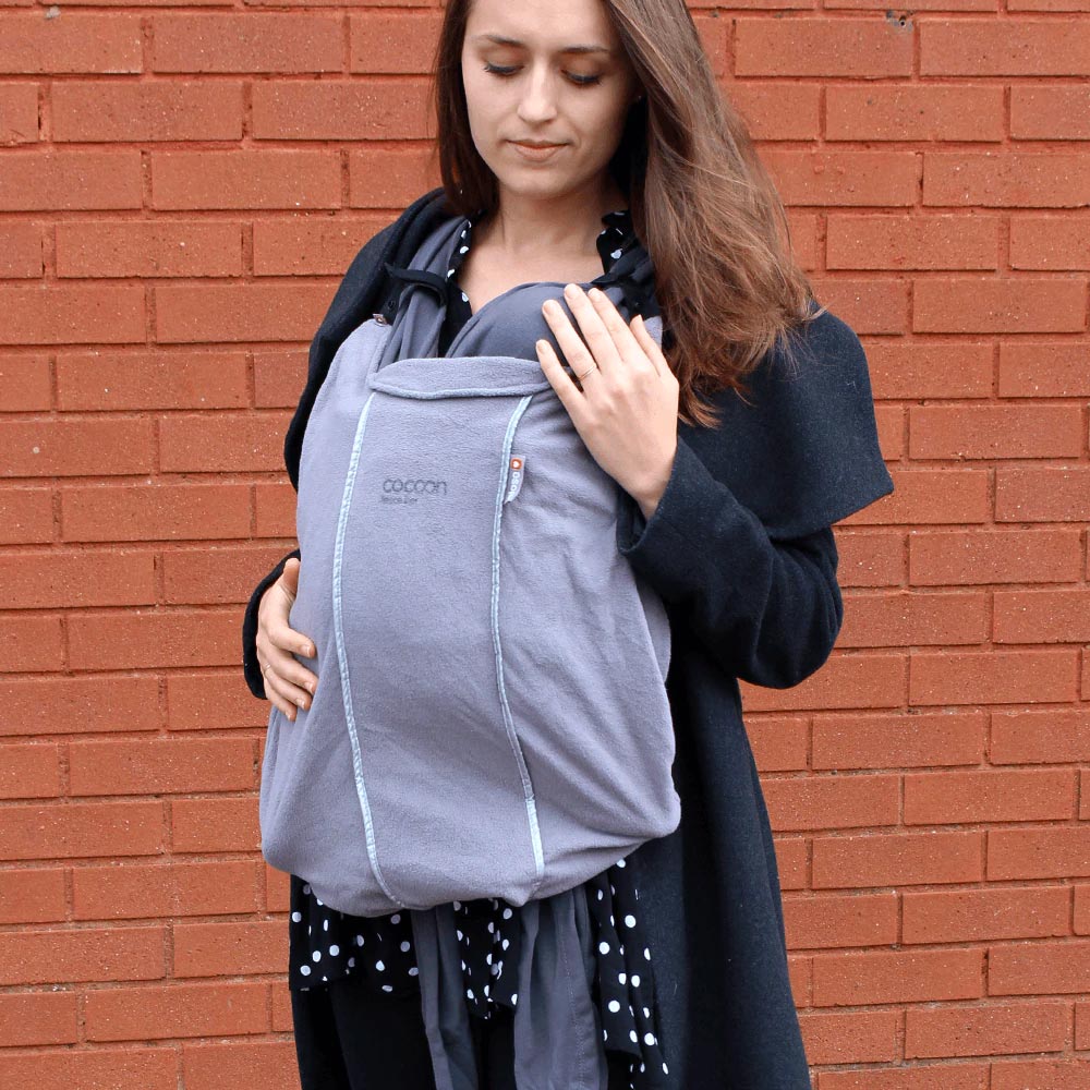 Woman stood in front of a brick wall wearing the close caboo baby carrier fleece cocoon liner