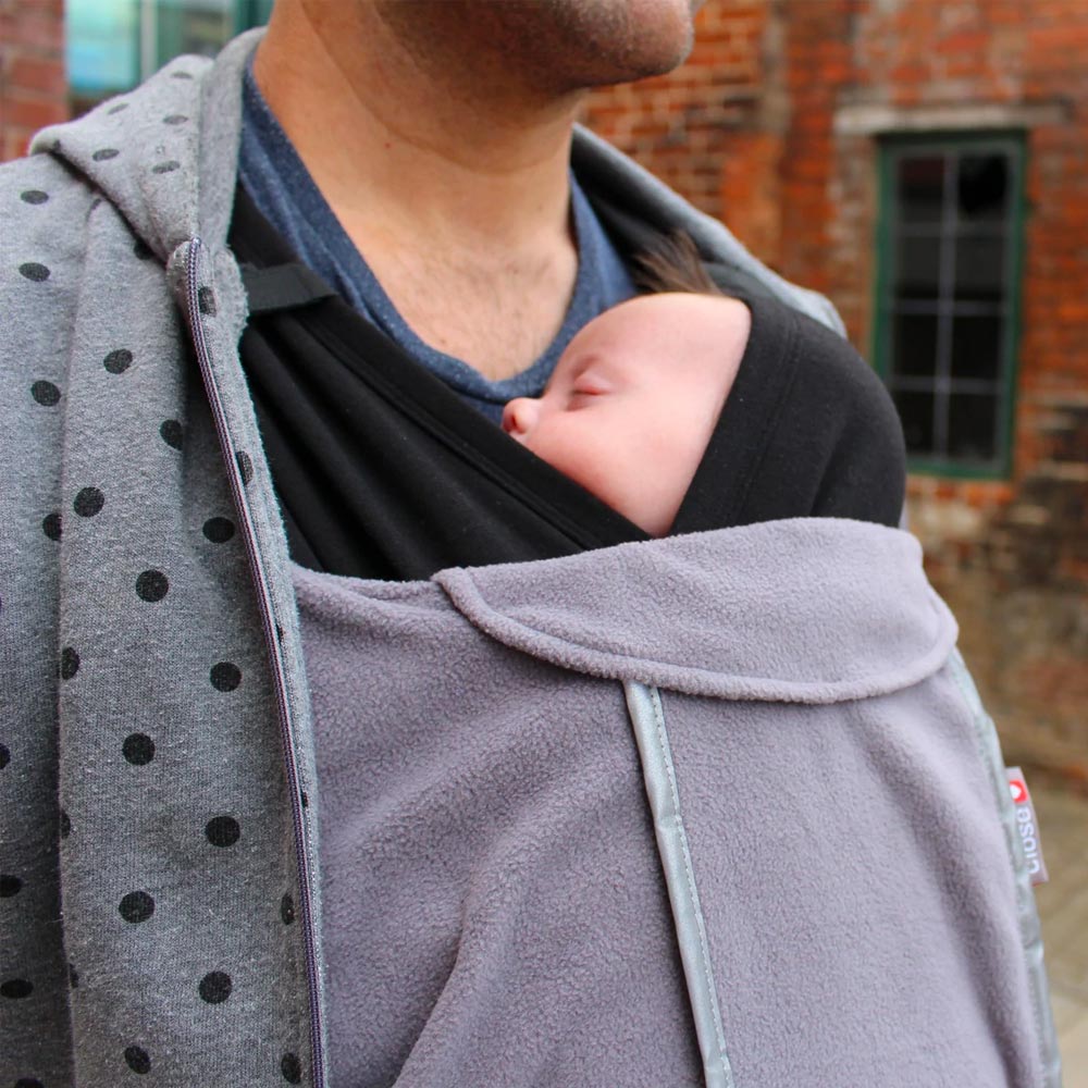 Close up of Man stood in front of a brick wall wearing the close caboo baby carrier fleece cocoon liner