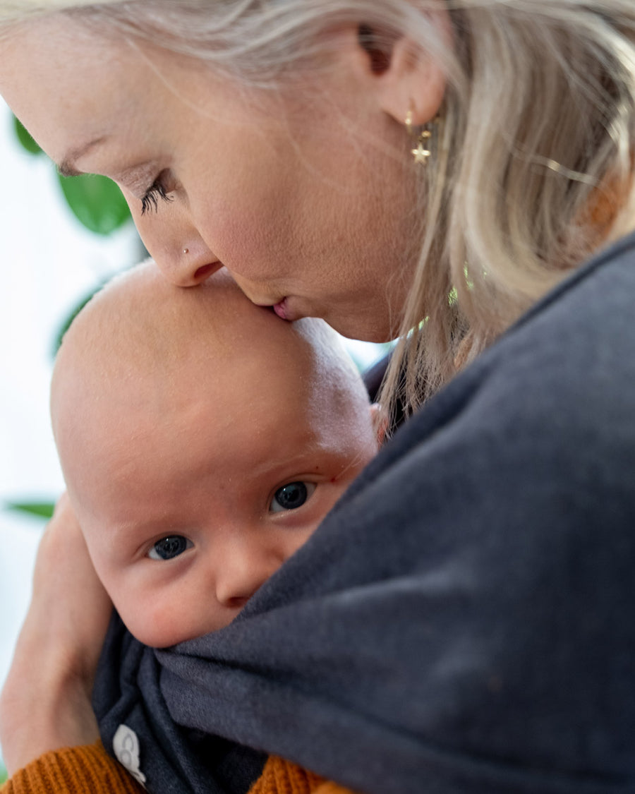 Close up of woman stood wearing the close caboo lite baby carrier in the nightfall colour