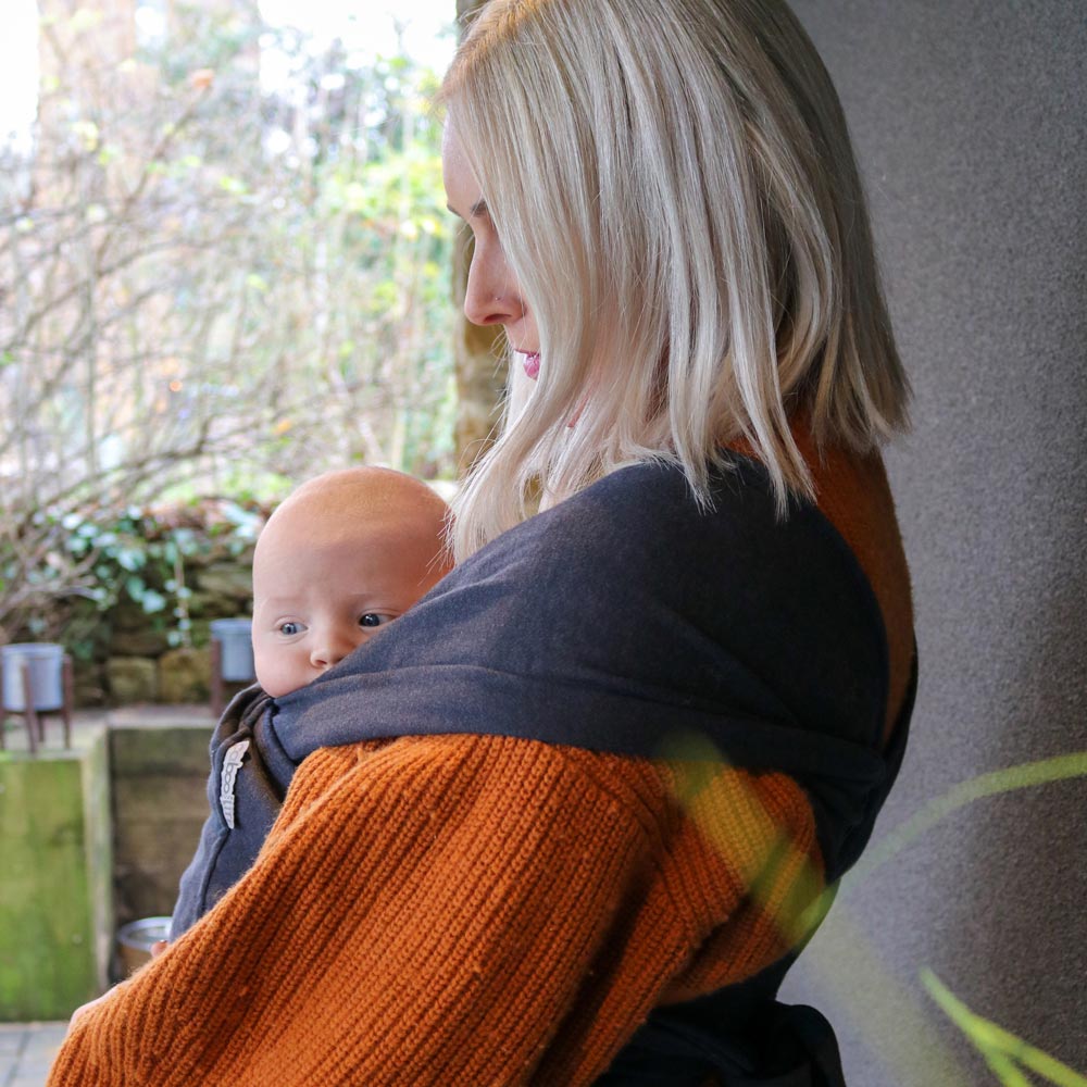 Close up of woman kissing the head of a baby in the close caboo lite baby carrier in the nightfall colour