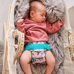 Sleeping baby wearing Pop-in light pink Ferret velcro Nappy Wrap with green trim details in a crib