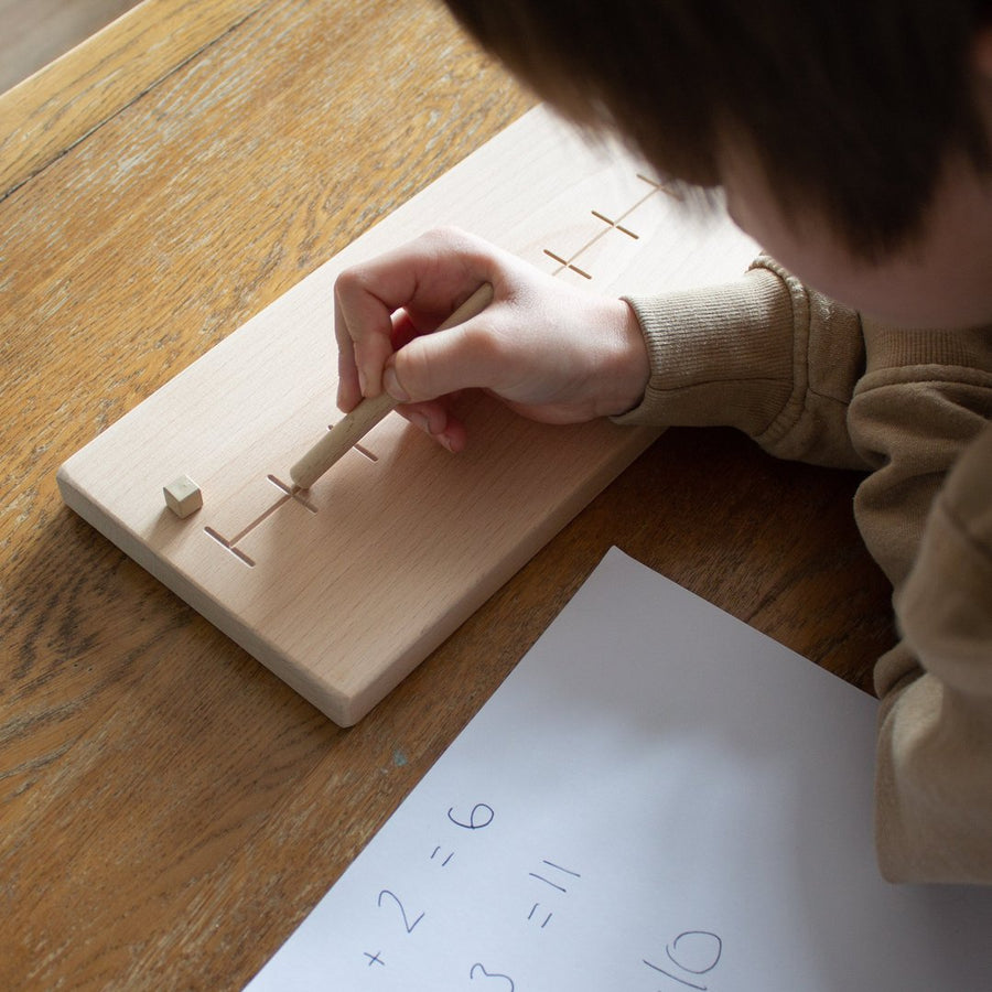 Child tracing over a Coach House handmade beech wood number line toy on a wooden table